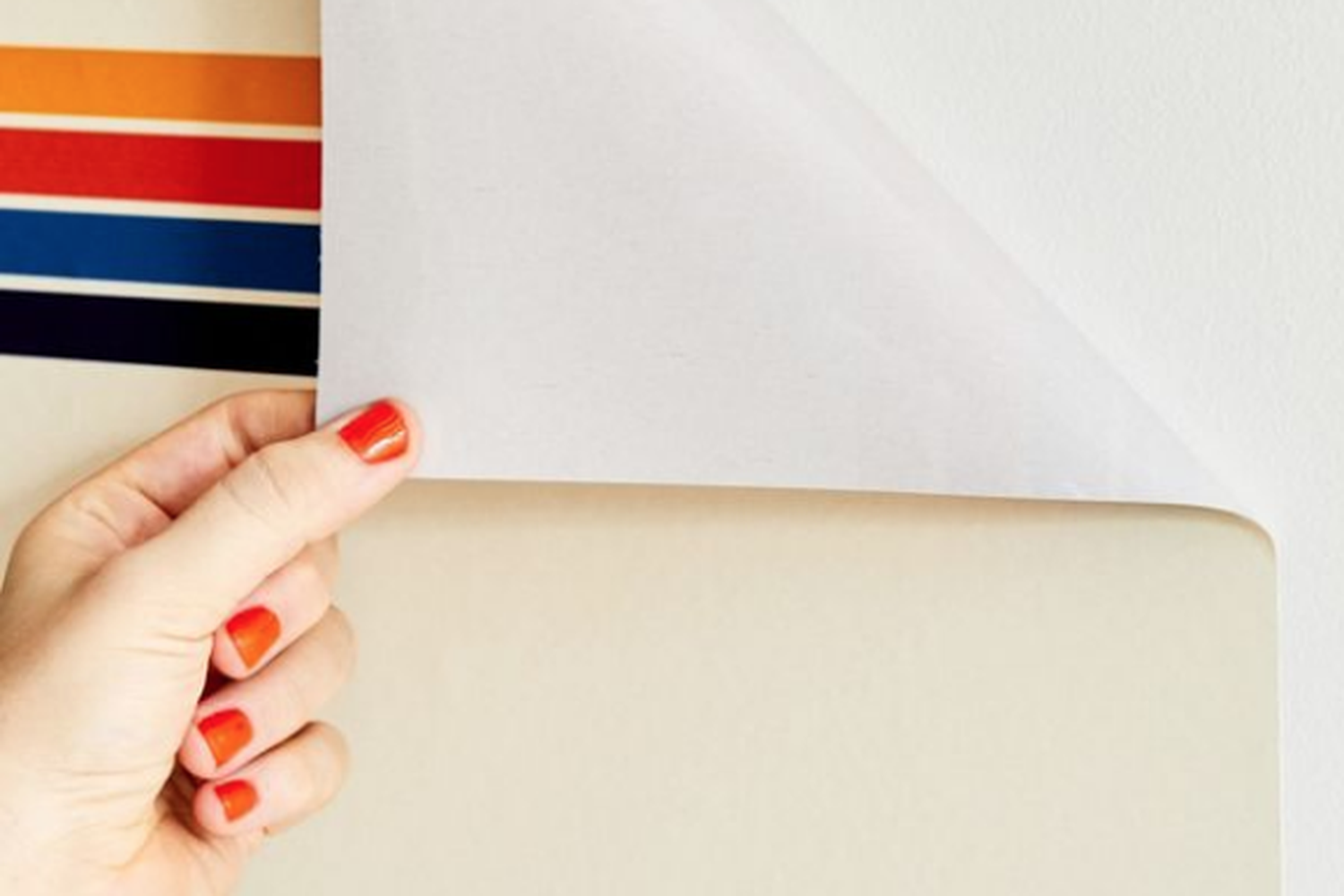 A person applying peel and stick striped wallpaper to a wall.