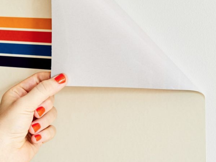 A person applying peel and stick striped wallpaper to a wall.