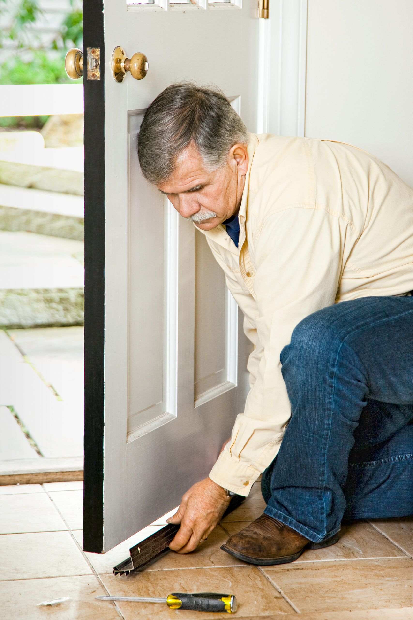 A man installing weatherstripping on the bottom of a door.