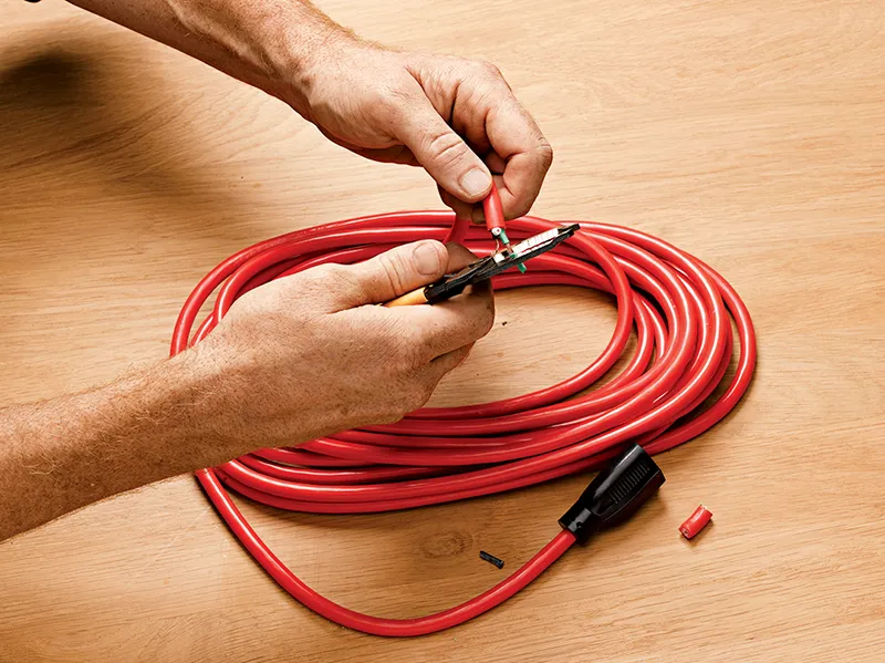 Hands using a wire stripper to remove the plug of a red extension cord.