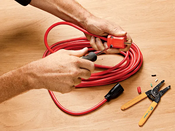 Hands using a screwdriver to secure the cover of a red extension cord plug.