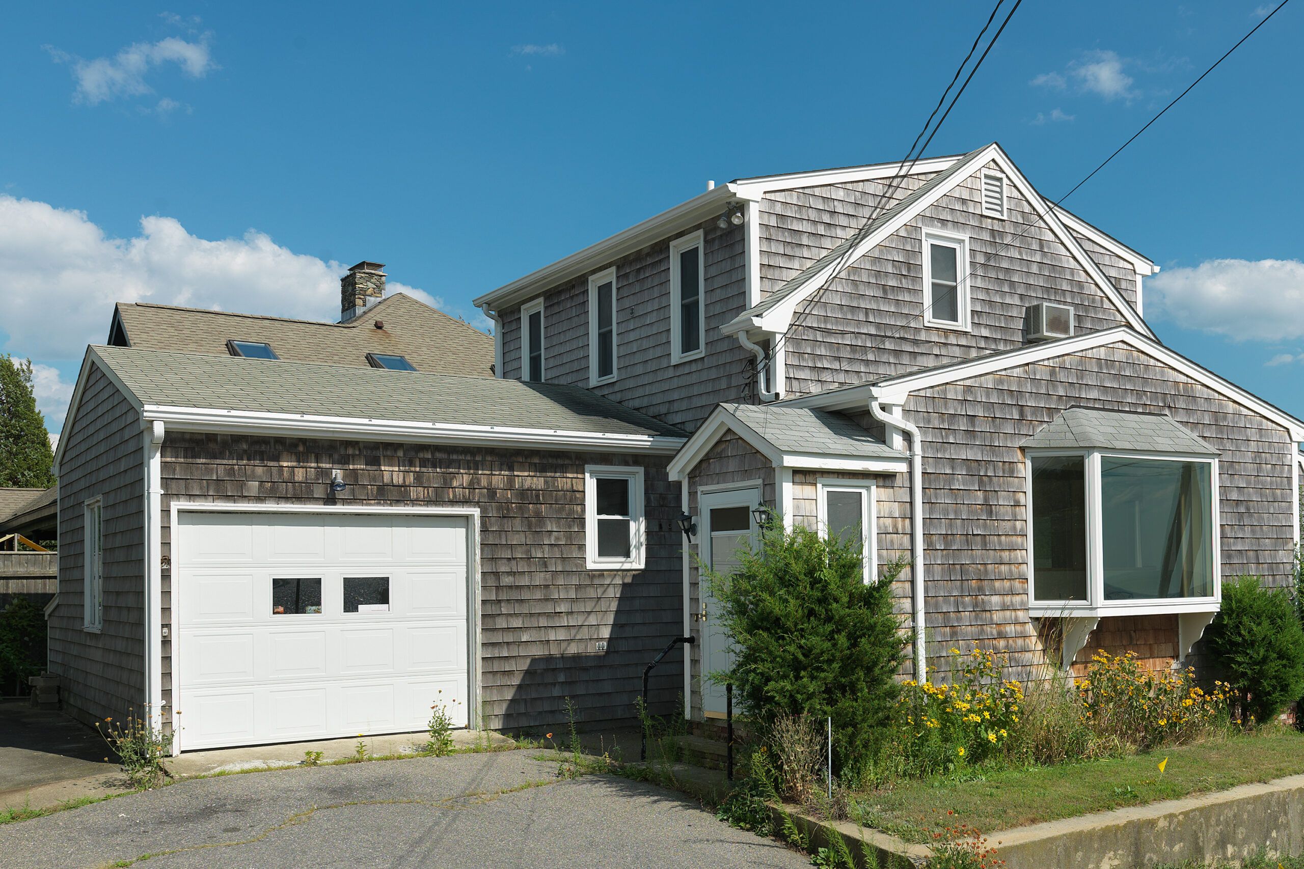 A grey home with a garage and flowers in front.