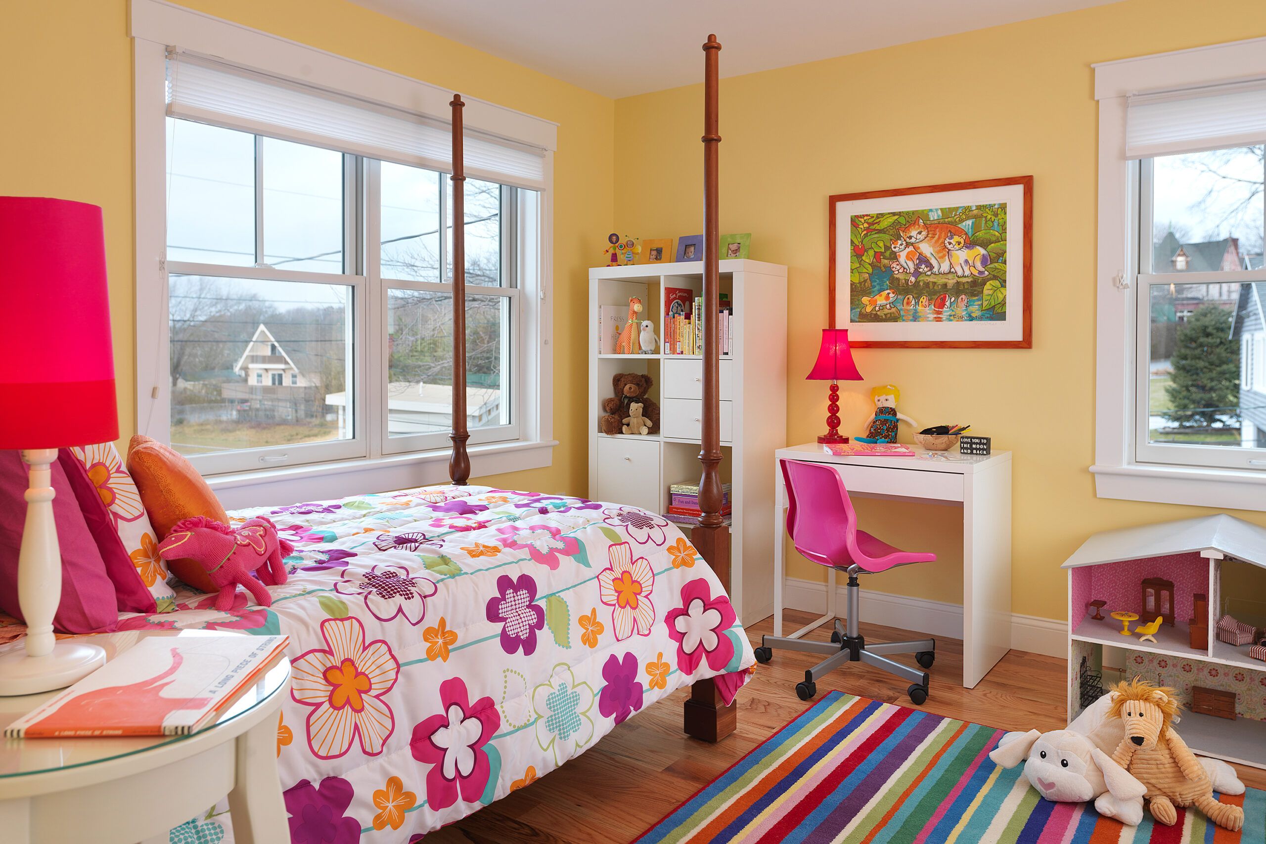 A bedroom with a colorful rug and bed comforter, stuffed animals are on the floor and on the bed.