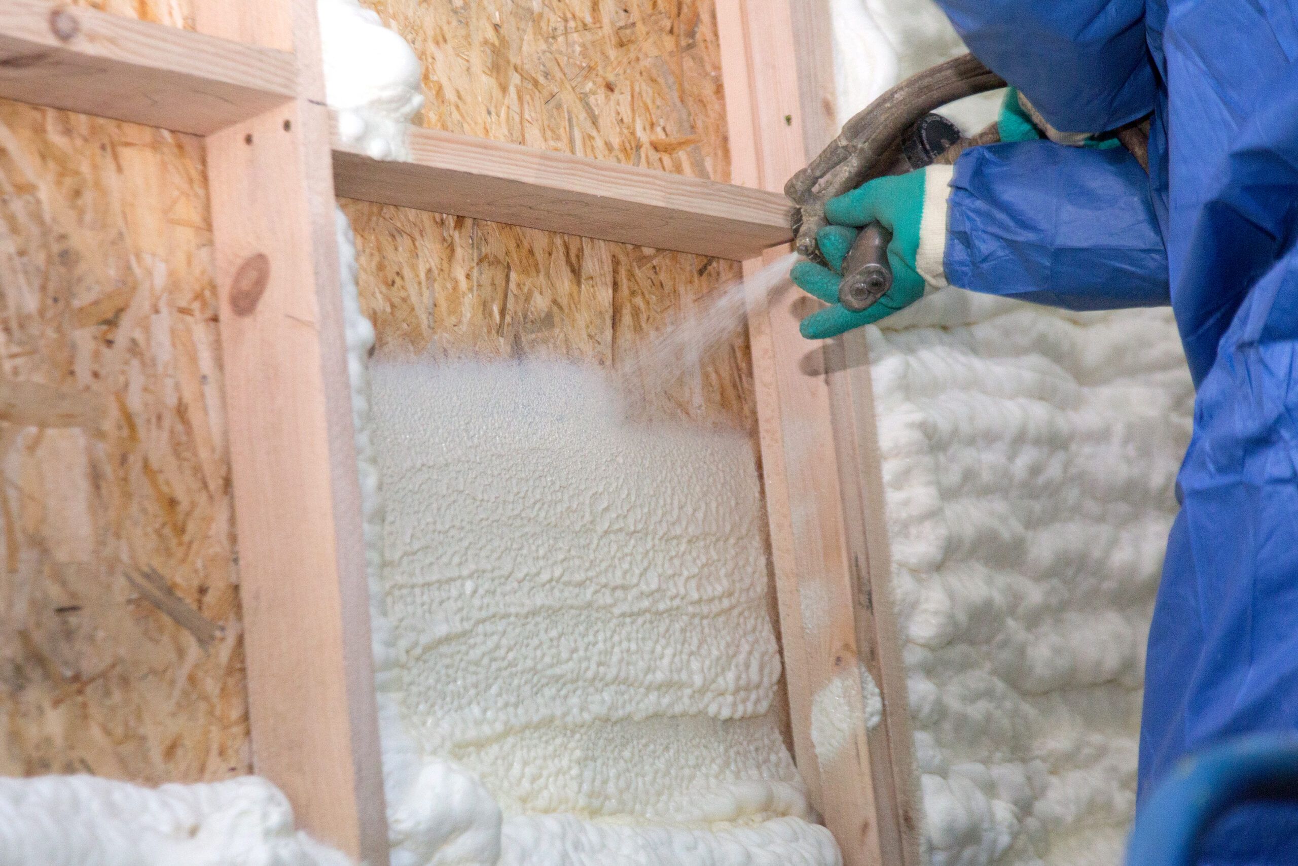 A man spraying a substance onto a board of wood in a garage addition.