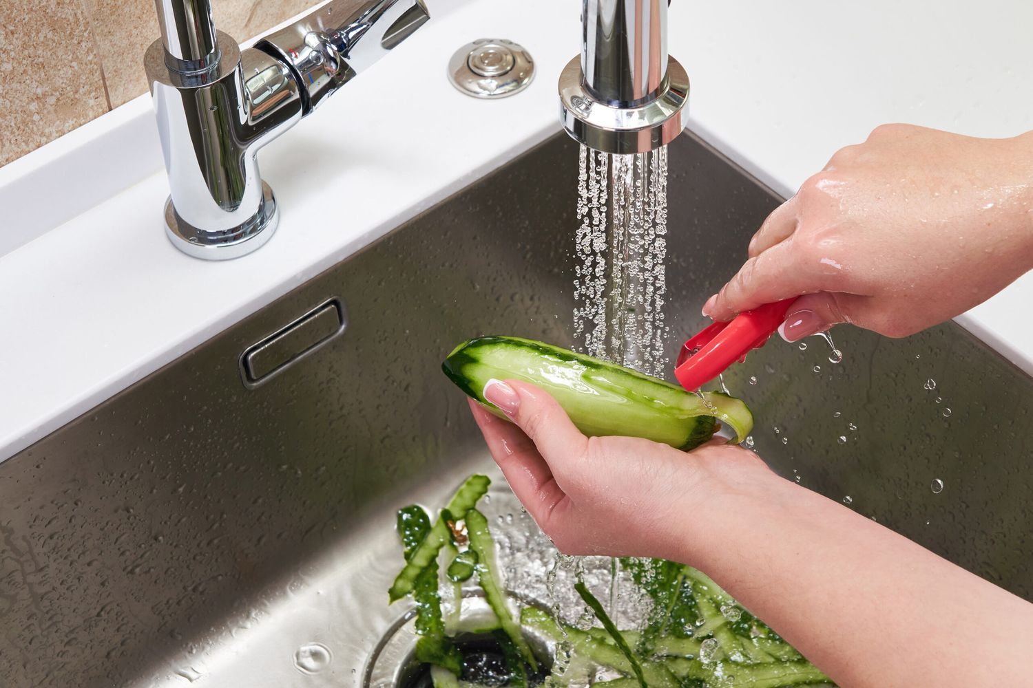 Cucumber is being peeled into a sink with a garbage disposal.