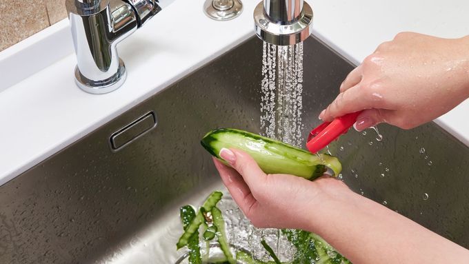 Cucumber is being peeled into a sink with a garbage disposal.