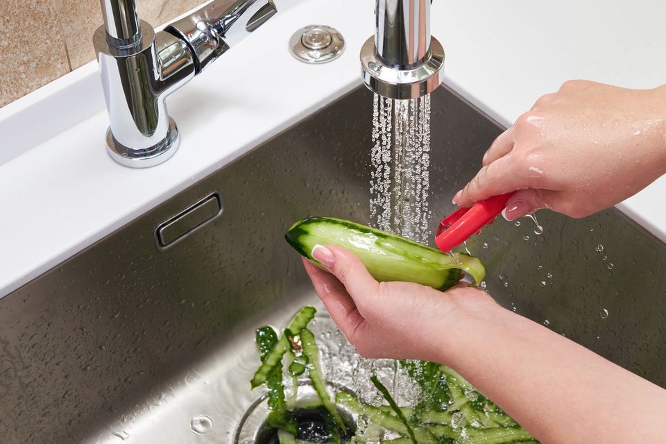 Cucumber is being peeled into a sink with a garbage disposal.