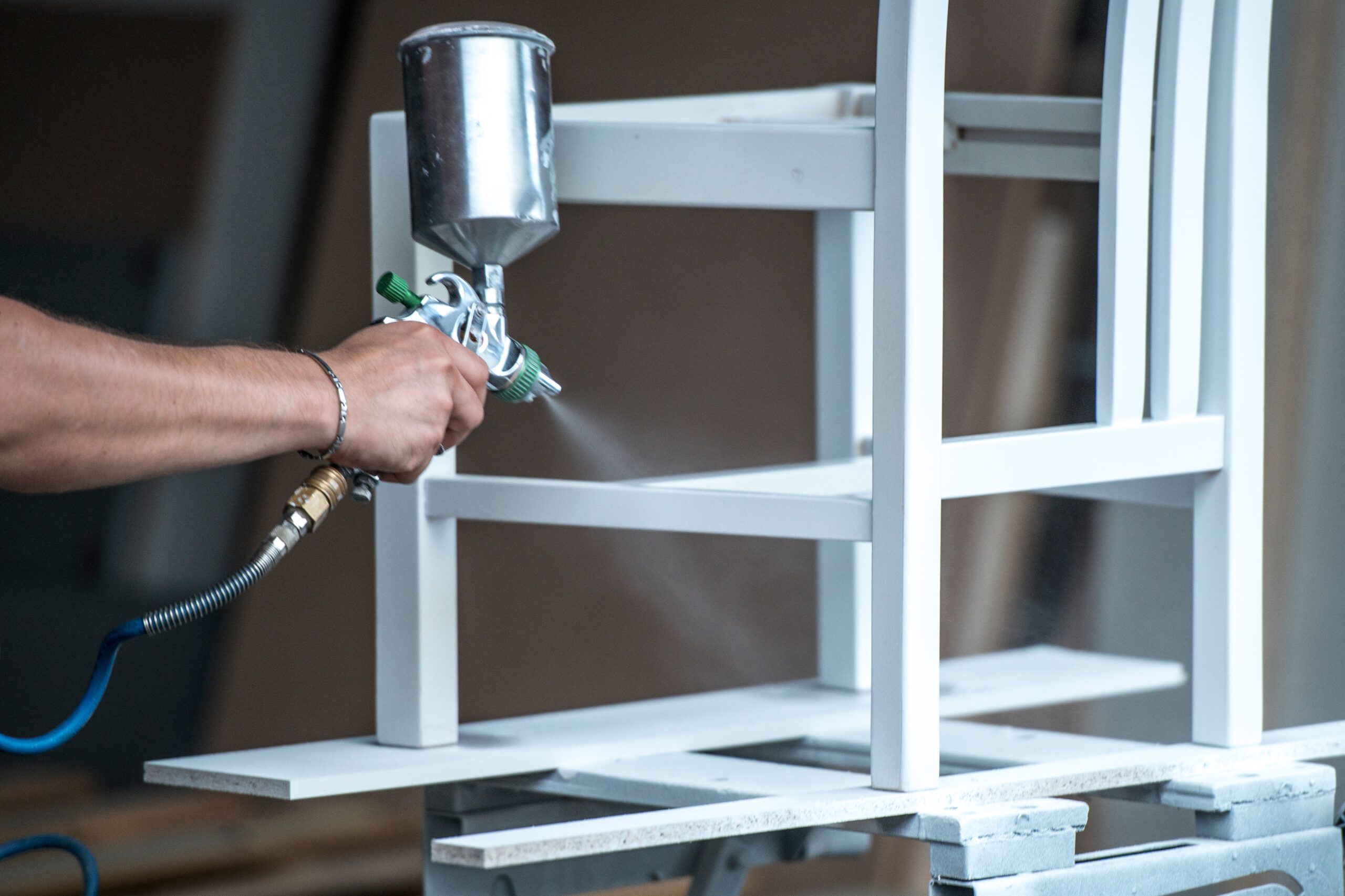 Side view of serious middle aged carpenter using spray gun for painting  wood detail with white