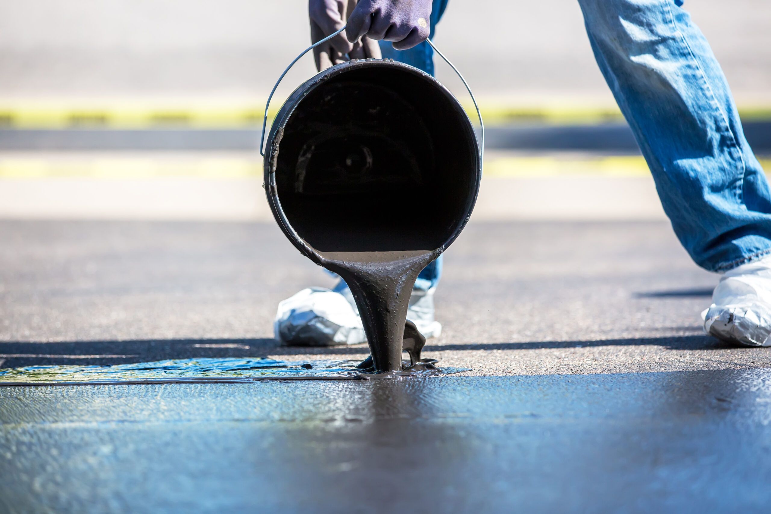 A person pouring sealant out on a driveway.