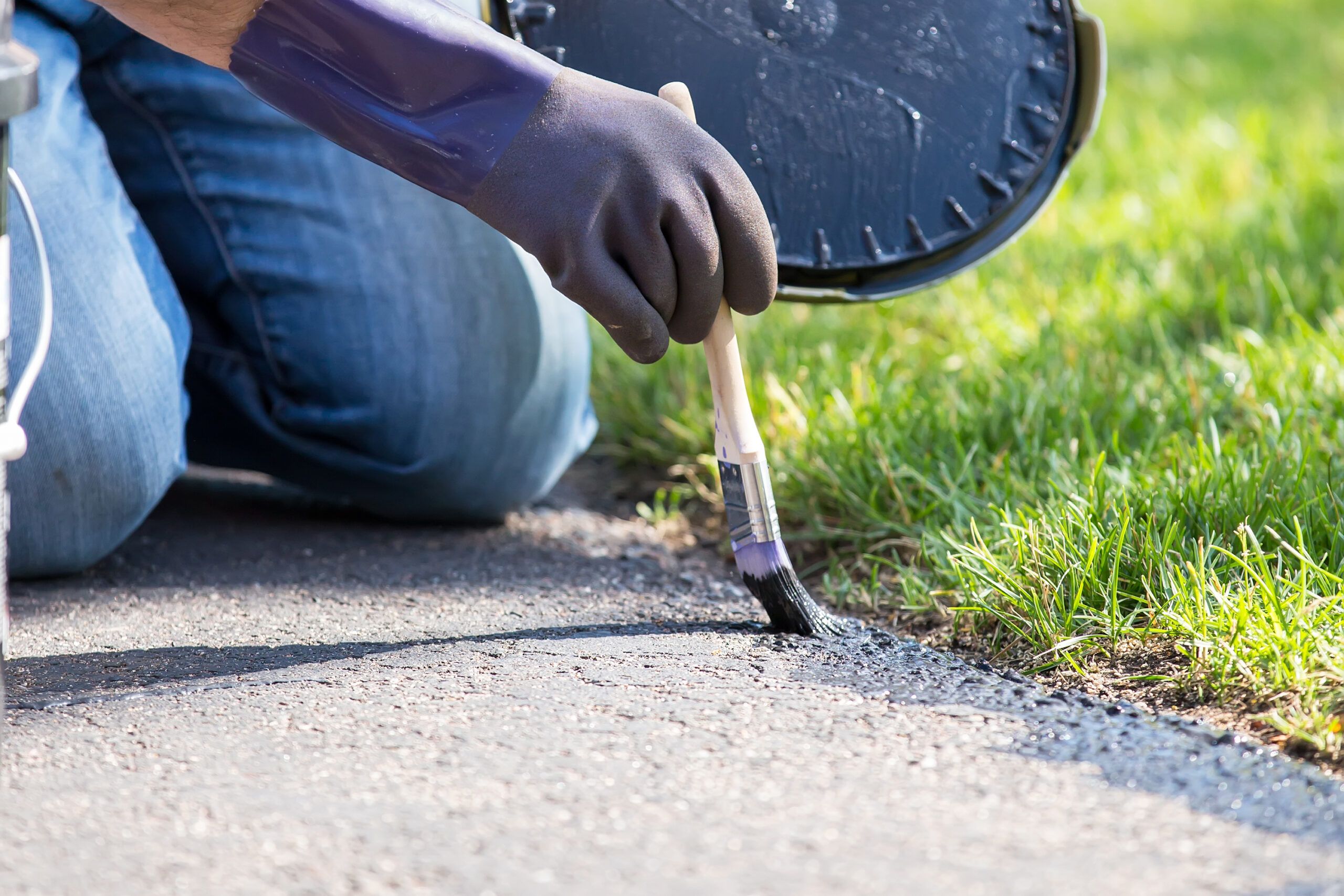 A person applying sealer to the edge of a driveway.