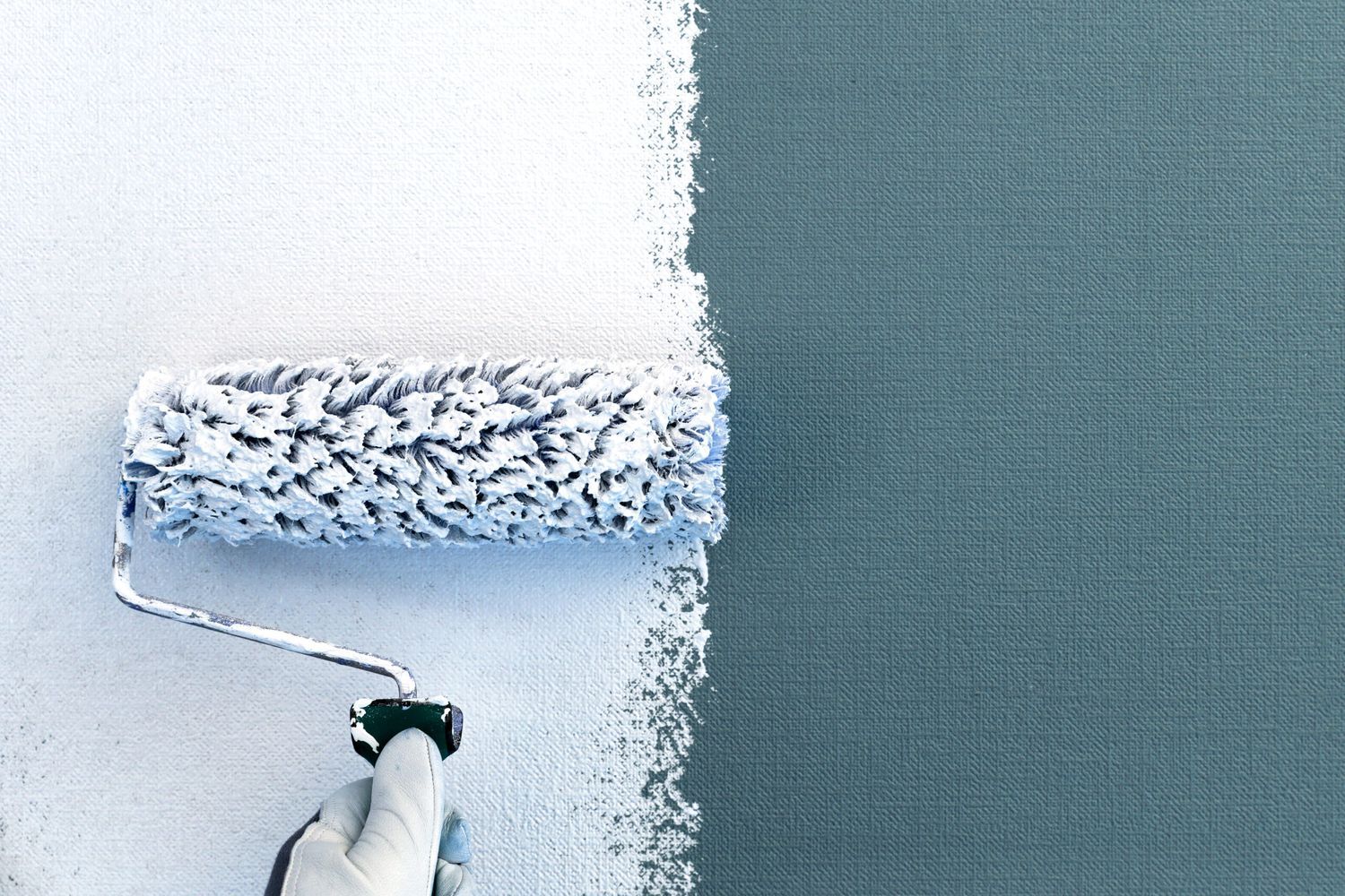 A person using a paint roller to paint over wallpaper in a house.