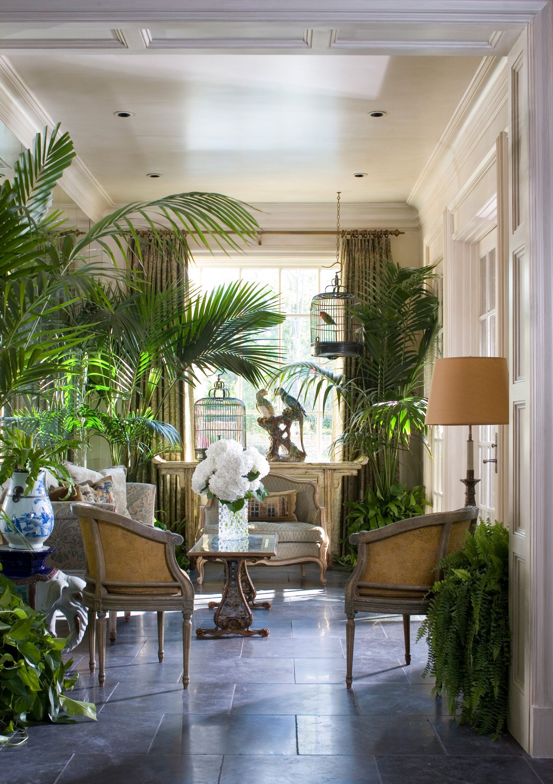 Image of a garden-inspired sunroom, including a large room with stone tile, seatings, and many plants 