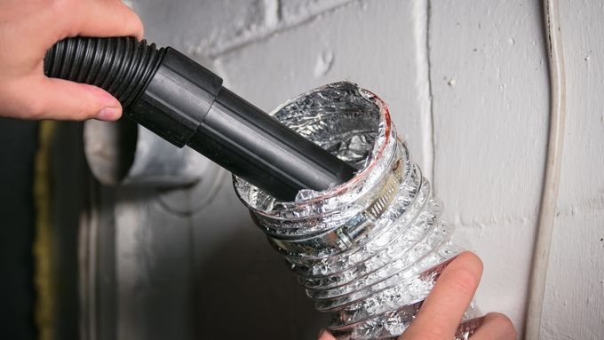 A person cleaning a dryer vent with a vacuum.