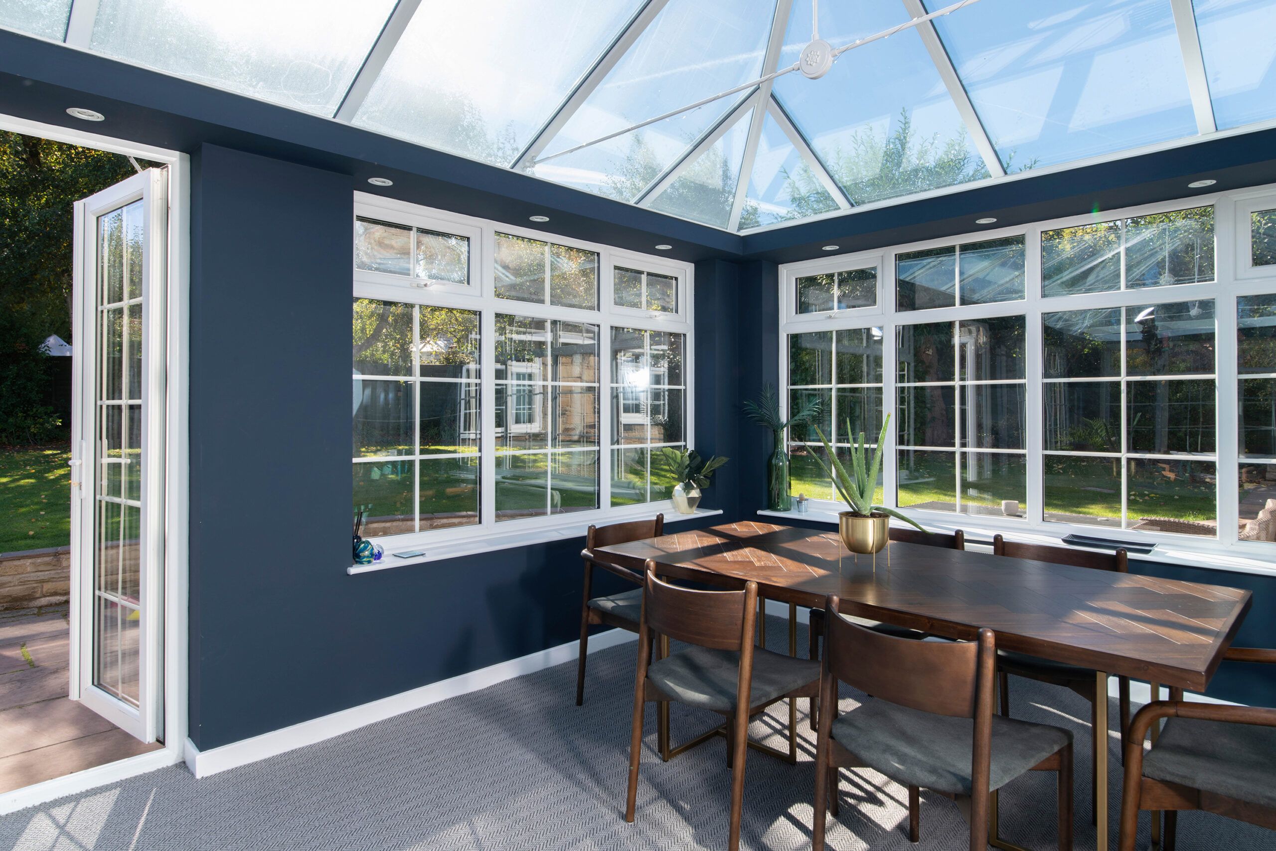 Image of a sunroom-turned dining room, complete with a dark wood dining table and chairs and dark blue painted walls