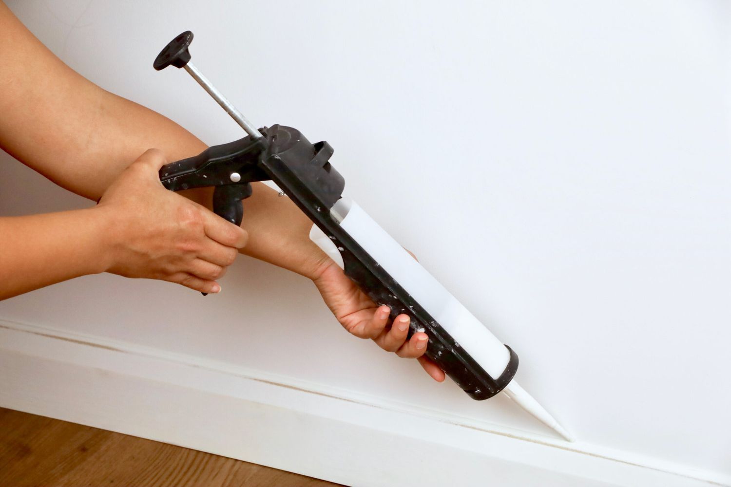 using a caulk gun to caulk around baseboards