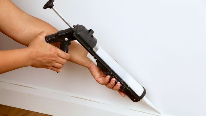 using a caulk gun to caulk around baseboards