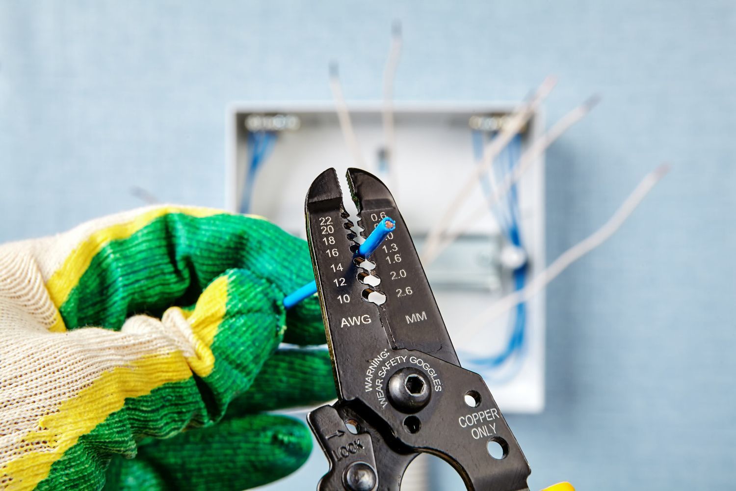 A man wearing gloves to strip an electrical wire.