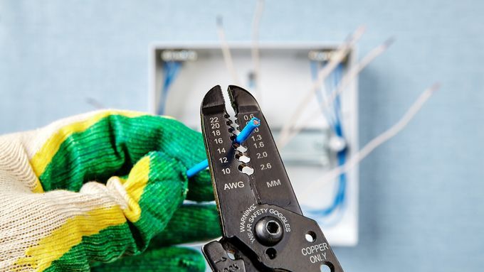 A man wearing gloves to strip an electrical wire.