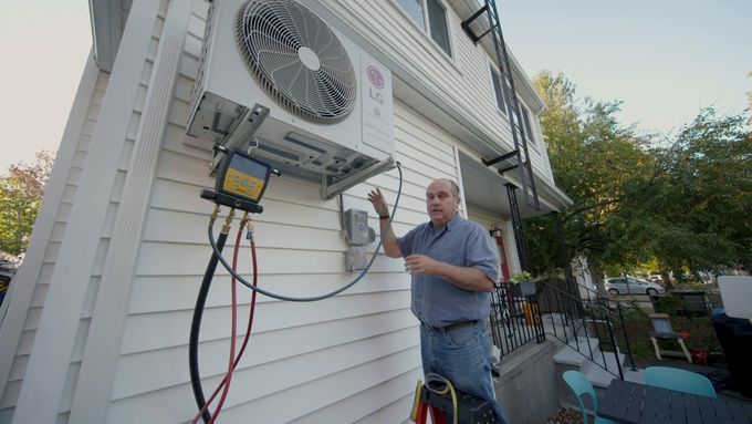 A man outside of a home working on a Mini-Split AC Heat Pump that is mounted on the home's siding.