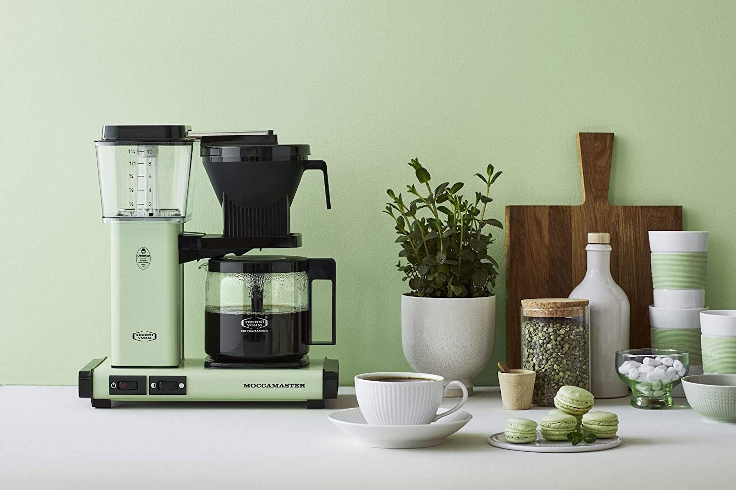Lead image for the best coffee maker guide. Lifestyle image of an automatic coffee maker on a white kitchen counter against a pale green wall.