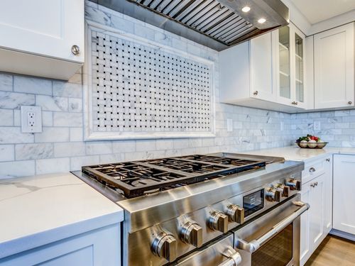Lifestyle image of a stainless-steel cooking range in a sparkling modern kitchen. Cover image for the This Old House Reviews Team's guide on how to remove scratches from stainless steel surfaces.