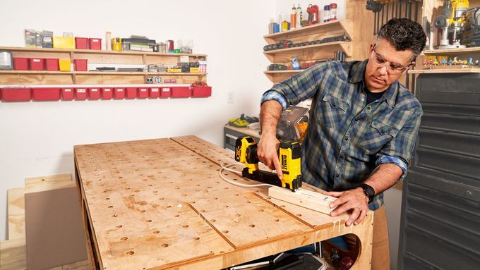 A man using a DeWalt Cordless Cable Stapler to apply staples to a cable over a block of wood.