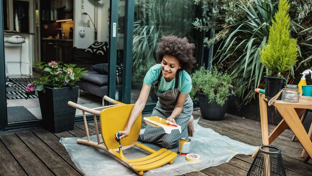 Woman painting a wooden chair yellow.