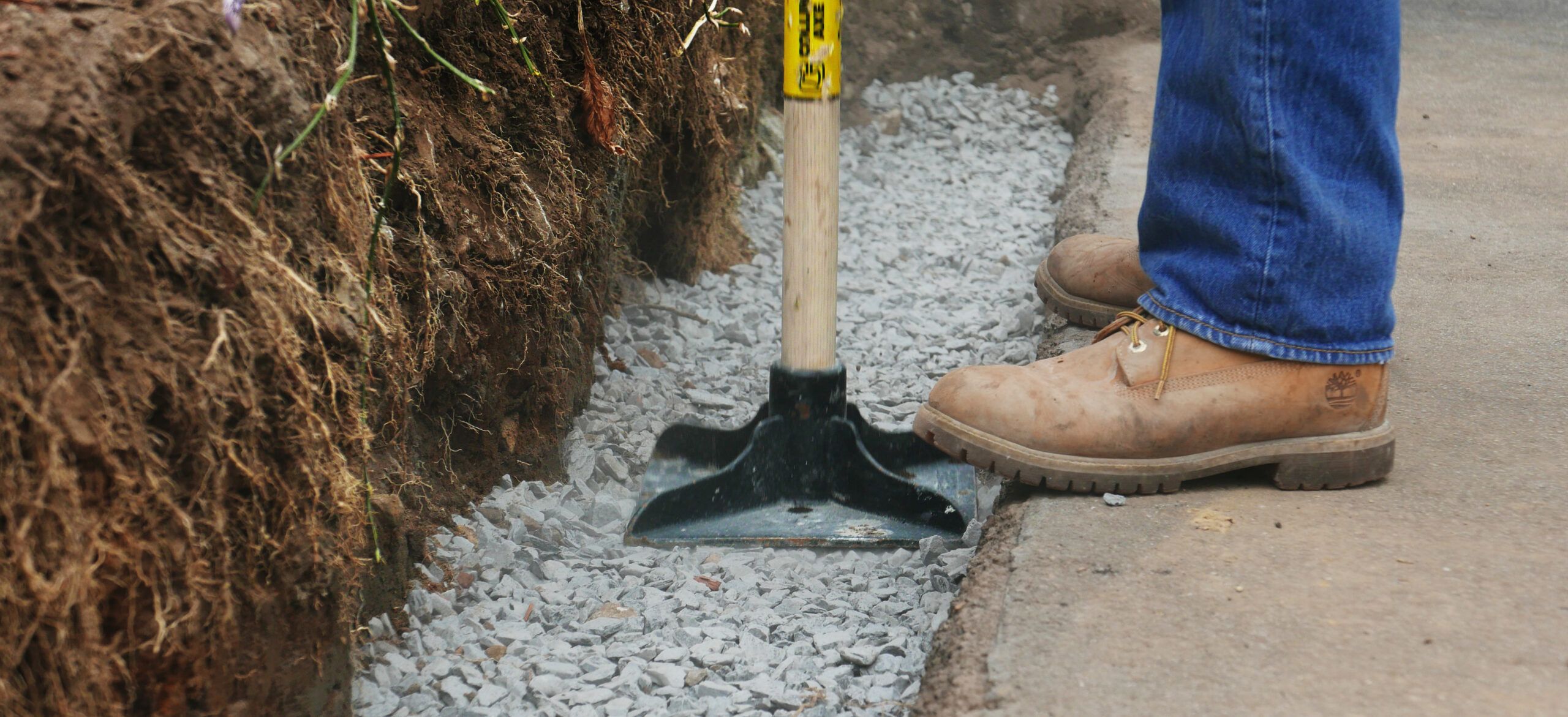 A person stamps down a gravel base to create a solid foundation for a concreate block retaining wall.