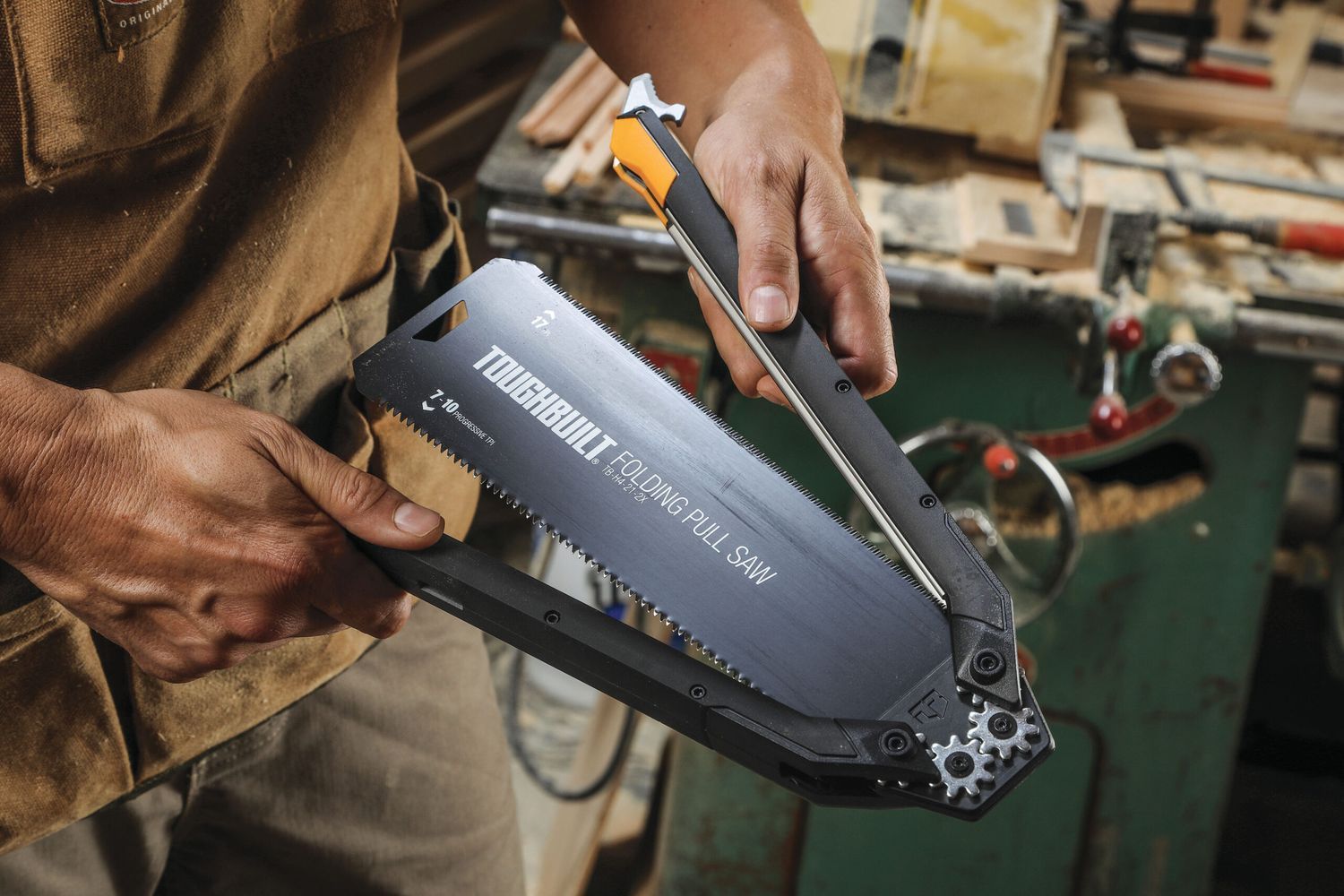 In a workshop, a person grips a ToughBuilt folding pull saw with a 12-inch blade, which is one of the best smart tools for DIY projects.