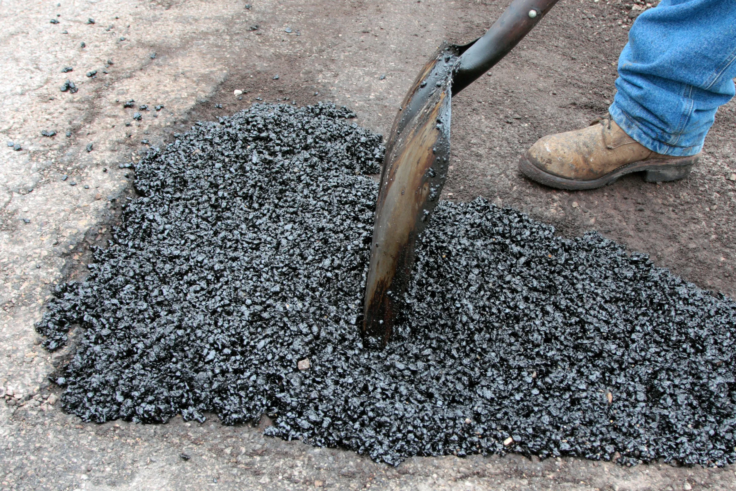 A damaged driveway having a pothole repaired by filling the hole with asphalt.
