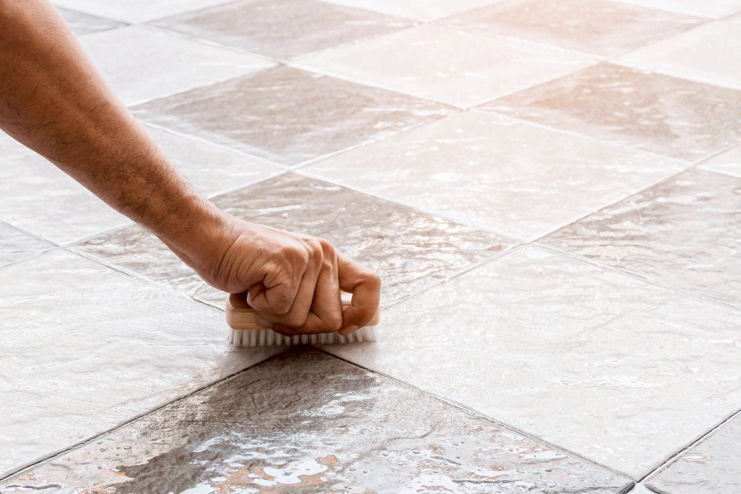 A person cleaning grout with a vinegar solution.