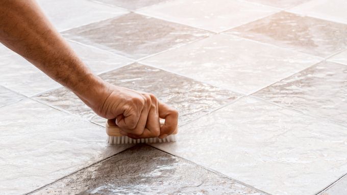 A person cleaning grout with a vinegar solution.