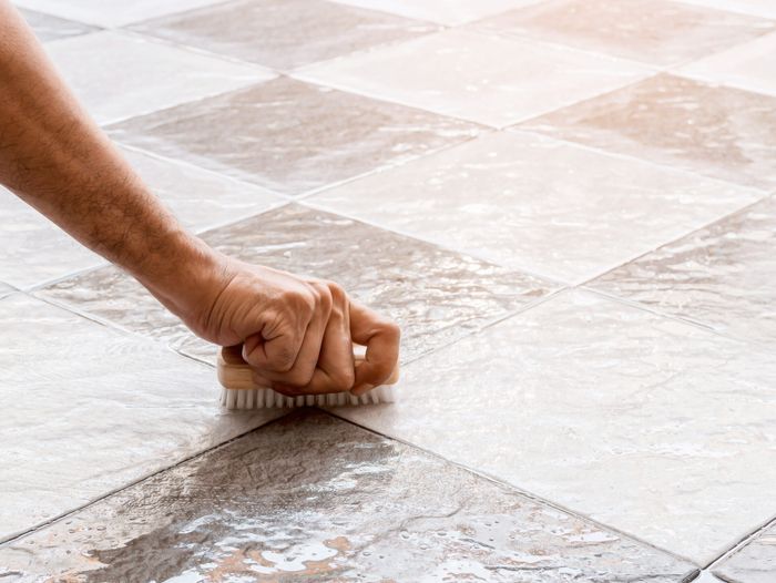 A person cleaning grout with a vinegar solution.