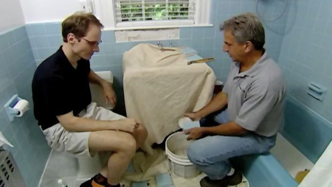 Two men sitting in a bathroom working on replacing wall tiles.