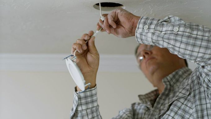 A man installing recessed lighting in the roof of a home.