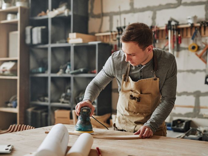 Man using electric sander in a woodworking workshop.