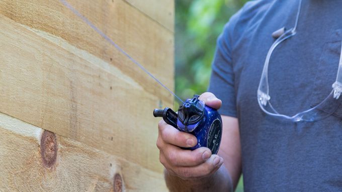 A man drawing a chalk line across a board of wood.