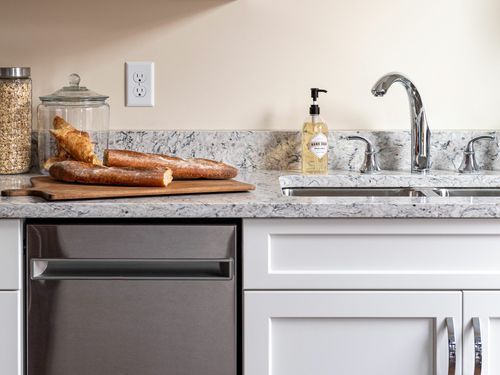 A decluttered kitchen with a sink and a cutting board with bread on top of it.