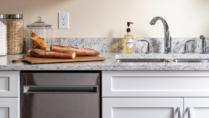 A decluttered kitchen with a sink and a cutting board with bread on top of it.