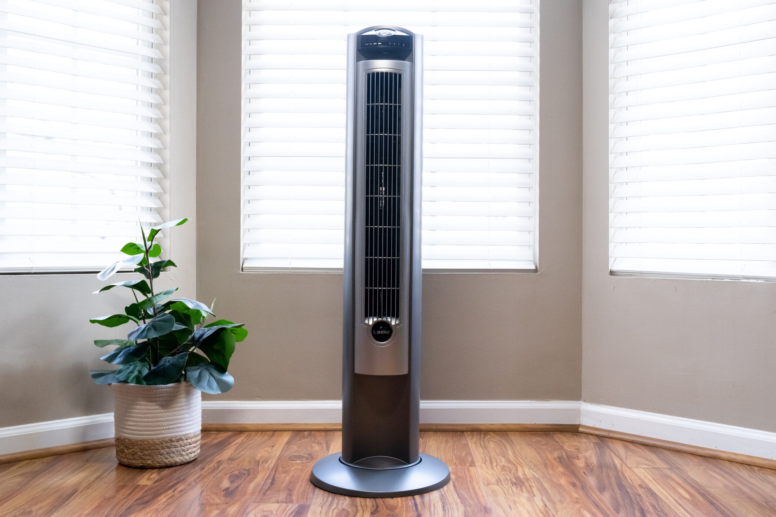 Lasko oscillating tower fan in front of a bay window, tan walls, and standing on a hardwood floor. Lead image for the best tower fan buying guide.