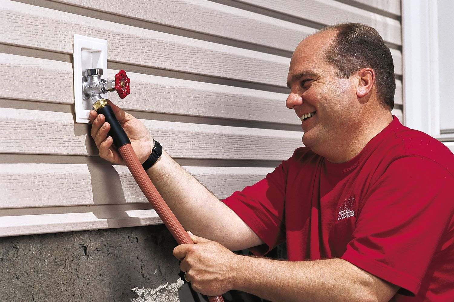 Richard Trethewey attaches a hose to a freezeproof faucet on the outside of a house.