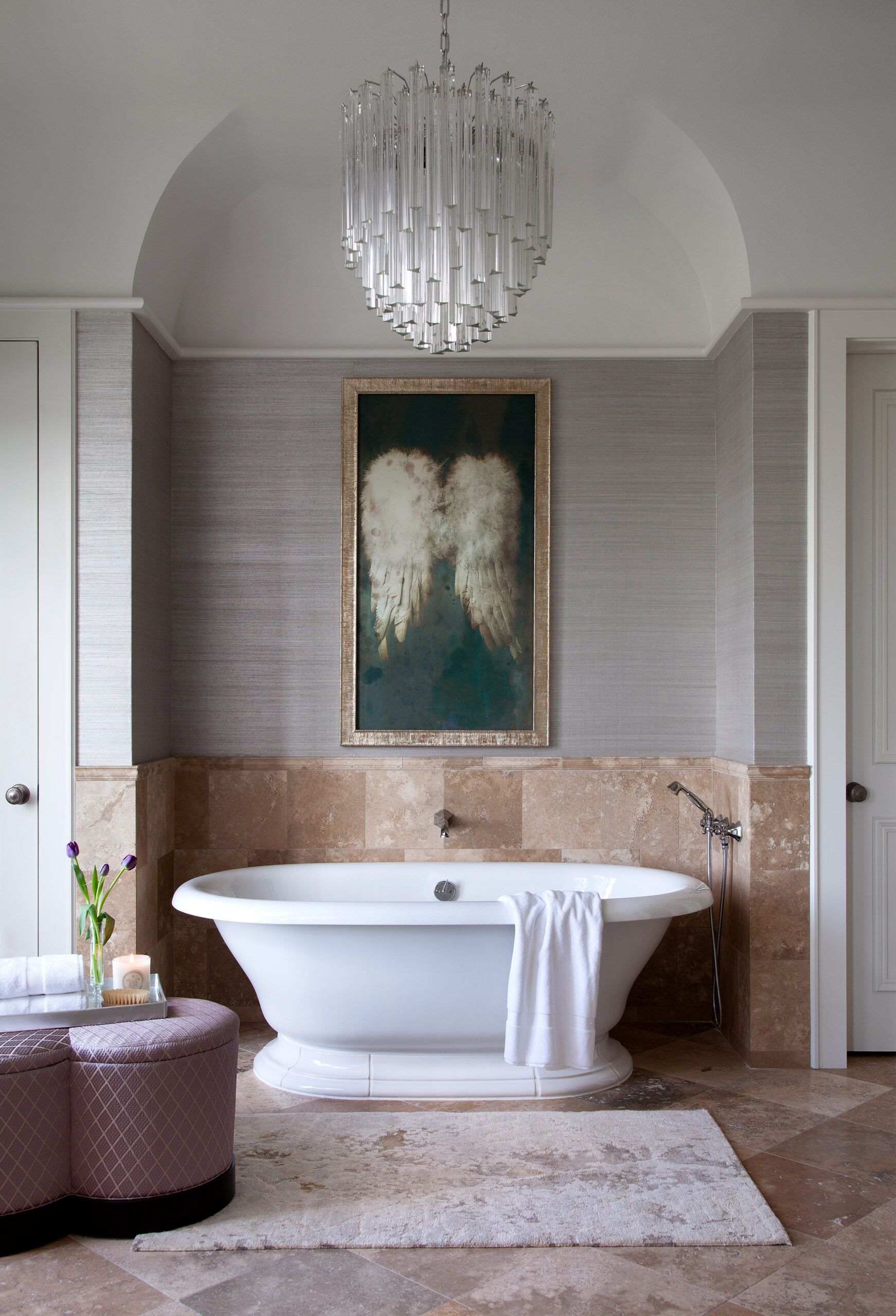 An elegant bathroom with a crystal bathroom chandelier, a freestanding bathtub, and a framed artwork above the tub.