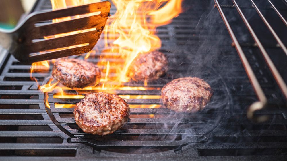 Burgers surrounded by flames cooking on a grill.