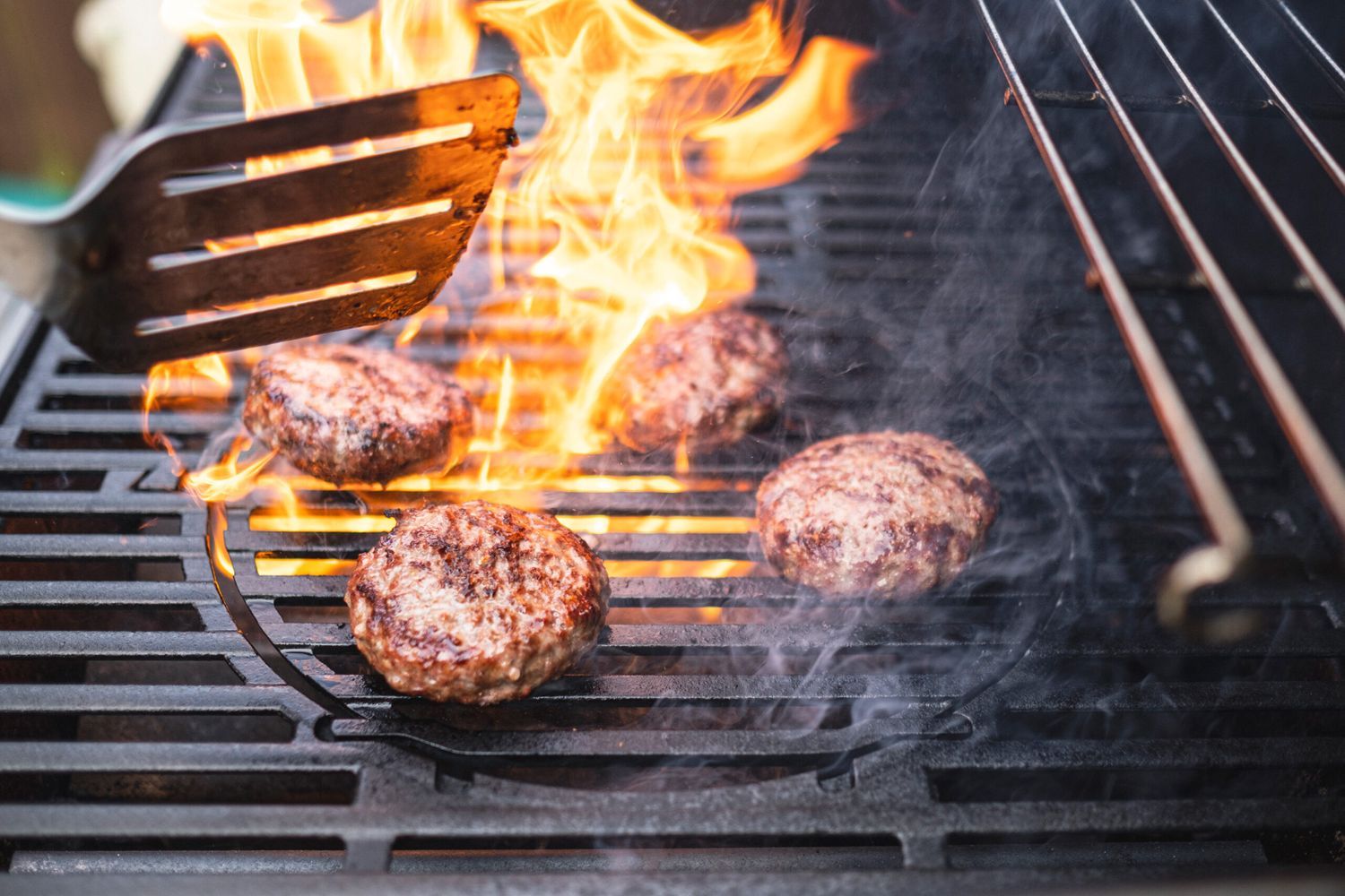 Burgers surrounded by flames cooking on a grill.
