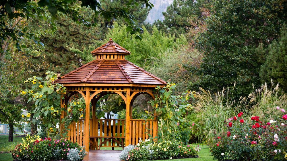 A wooden gazebo surrounded by grass and plantlife.