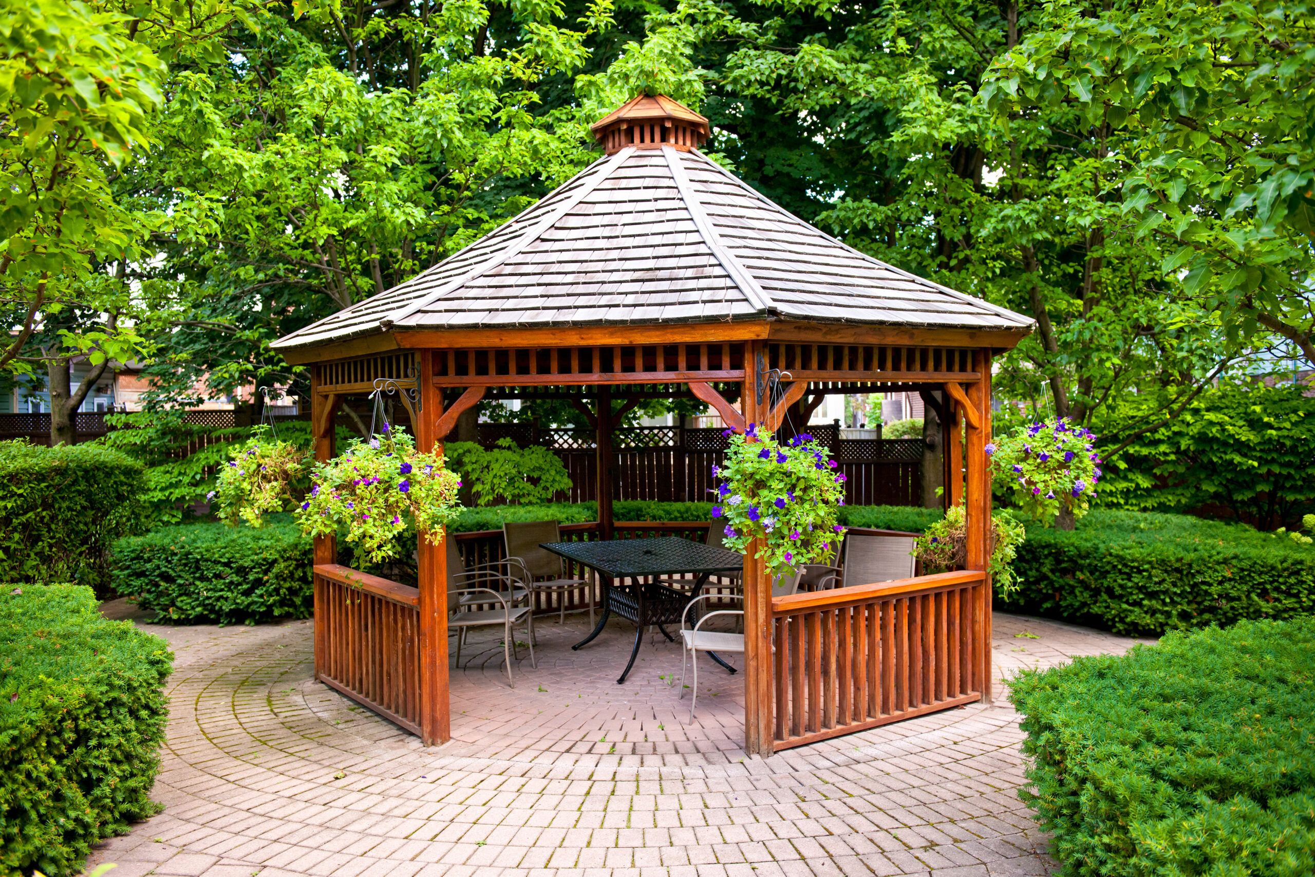 A gazebo on a brick path surrounded by flowers and bushes.