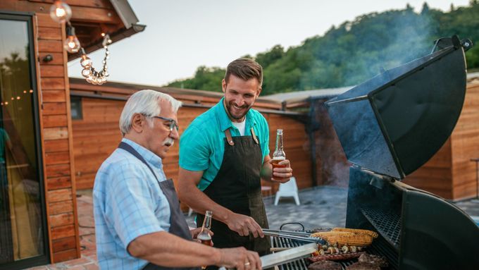 An older and a younger man grilling together on deck in the mountains. Lead image for Father's Day Gift Guide; best father's day gifts.