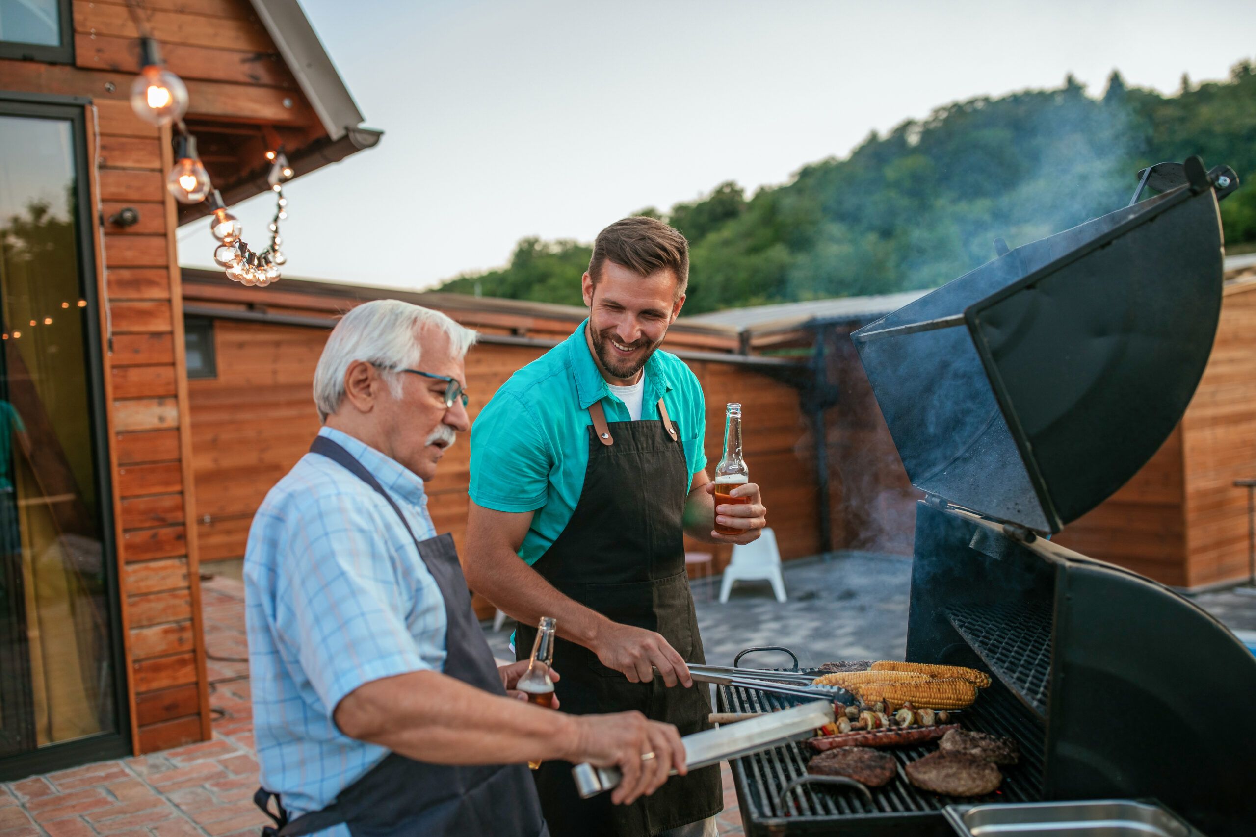 An older and a younger man grilling together on deck in the mountains. Lead image for Father's Day Gift Guide; best father's day gifts.