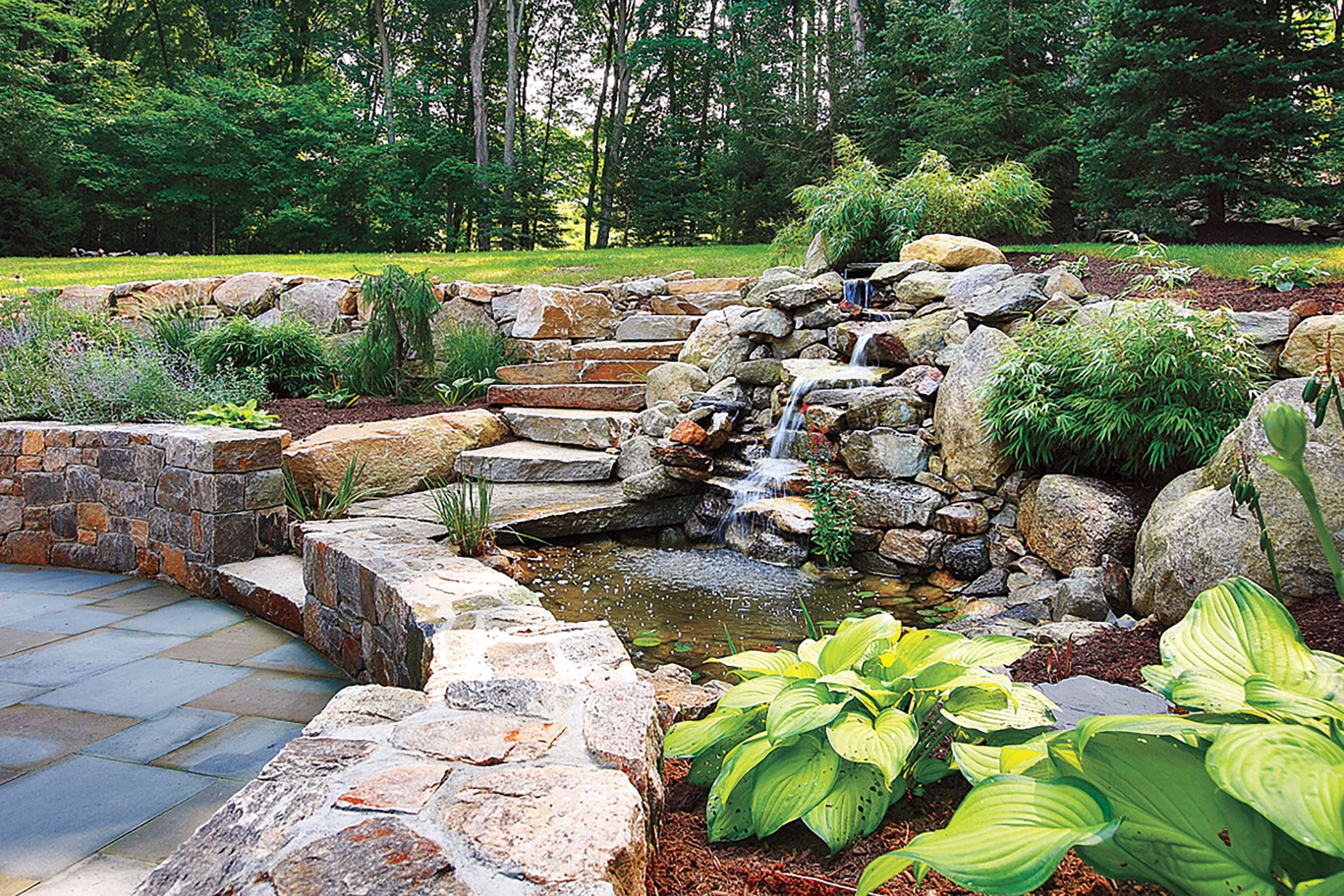 Water flowing down a set of rocks into a backyard pond beside leafy green plants.