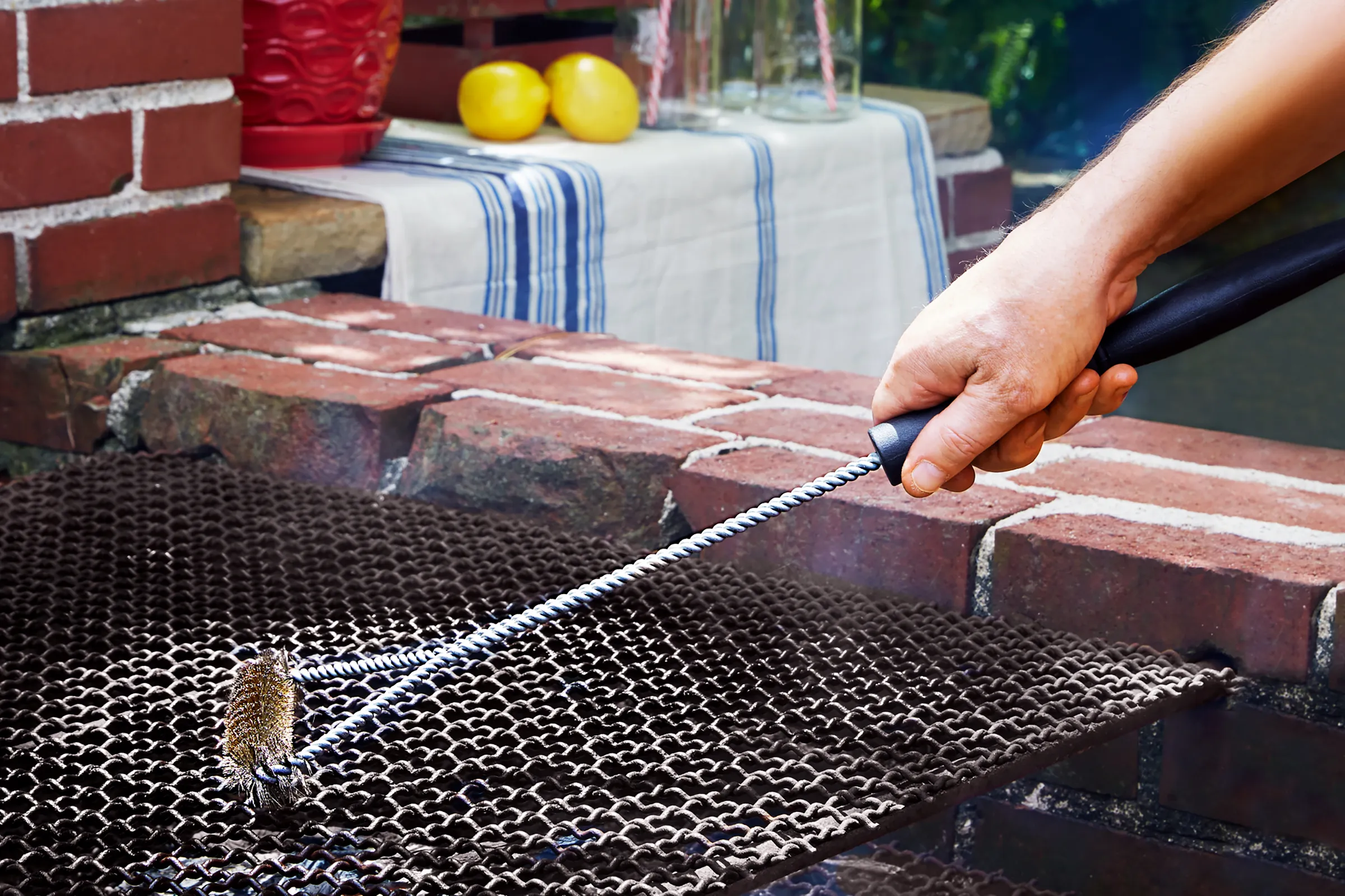 A man using a brush to clean the surface of a brick barbecue pit.